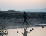 Охотник в вейдерсах идет по берегу водоема осматривая чучела уток